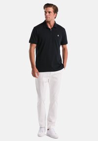 Marineblauwe polo met een kraag, korte mouwen en geborduurd logo. Gecombineerd met witte broek en witte sneakers, voor een casual stijl.