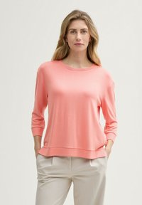Maglione in cotone morbido di colore corallo chiaro, con scollatura rotonda e maniche a tre quarti. Presenta una vestibilità comoda e un dettaglio discreto all'orlo.