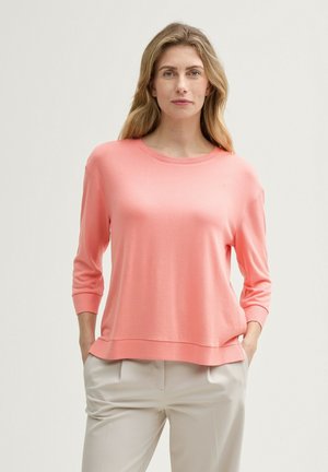 Maglione in cotone morbido di colore corallo chiaro, con scollatura rotonda e maniche a tre quarti. Presenta una vestibilità comoda e un dettaglio discreto all'orlo.