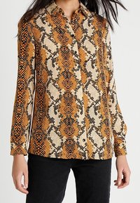 Camicia button-up con stampa di serpente nei colori arancione, nero e crema. Maniche lunghe, colletto e tessuto testurizzato.
