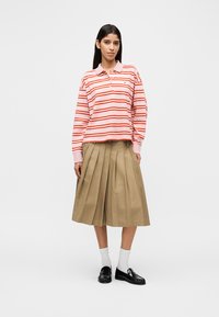 Ριγέ ροζ και κόκκινο μπλουζάκι πόλο με μακριά μανίκια και γιακά, σε συνδυασμό με μπεζ φούστα με πιέτες. Μαύρα μοκασίνια και λευκές κάλτσες ολοκληρώνουν την εμφάνιση.