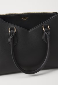 Black tote bag with a textured finish, gold zipper, and dual top handles. The interior is spacious with a logo label visible.