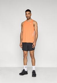 Ανδρικό πορτοκαλί αμάνικο τοπ με στρογγυλή λαιμόκοψη, συνδυασμένο με μαύρο σορτς. Διαθέτει αντανακλαστικό λογότυπο και πλαϊνές πινελιές.