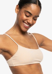Licht perzikkleurige geribbelde bikini-top met dunne banden, voorzien van een gestructureerd ruitpatroon en een naadloos ontwerp. Geschikt voor zwemkleding.