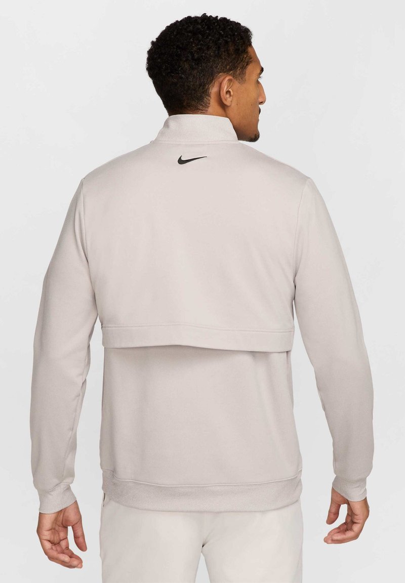 Hellgrauer Nike-Pullover mit hohem Kragen, Rückenüberlagerung, gerippten Bündchen und kleinem schwarzem Logo am Hals. Glatte Textur, lässige Passform.