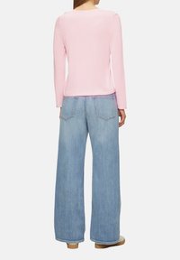 Helles rosa Langarmoberteil mit Rundhalsausschnitt, kombiniert mit weit geschnittenen, hellblauen Jeans aus Denim, die über Rückentaschen und eine lockere Passform verfügen.