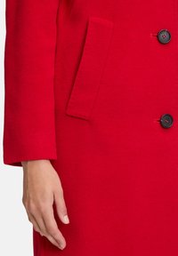 Hand rustend naast de zak en knopen op een felrode wollen mouw en voorkant van een jas.