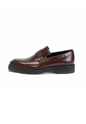 Brown leather loafer with black rubber sole, moc toe stitching, and decorative strap across the front, shown from the side on a white background.