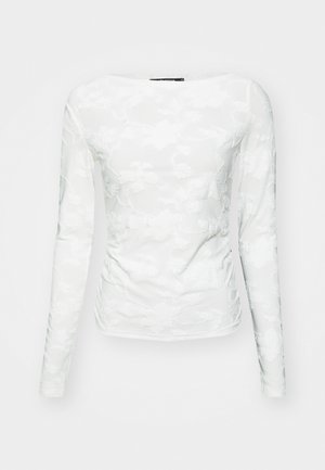 Haut à manches longues blanc en tissu texturé, doté de motifs en dentelle florale et d'un col en rond, forme ajustée mettant en valeur la silhouette.