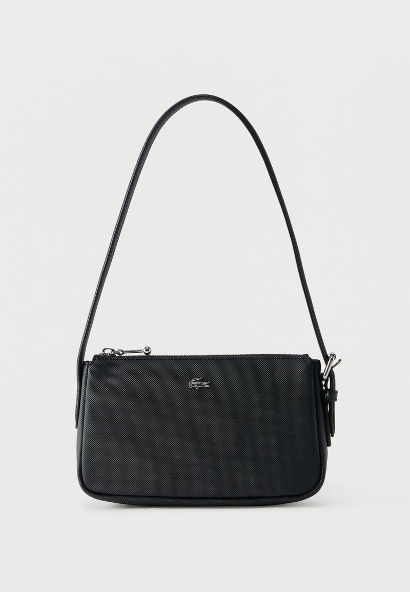 Μαύρη υφασμάτινη τσάντα ώμου με ασημένιο φερμουάρ και μικρό ασημένιο λογότυπο κροκοδείλου στο μπροστινό μέρος, με φόντο απλό.