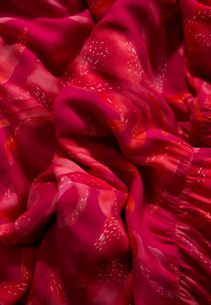 Silk fabric in vibrant pink with abstract patterns in red and white. Features soft texture and gathered edge detail.
