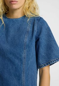 Lys blå denim topp med rund hals, korte ermer og synlige sømdetaljer. Glatt tekstur med en avslappet passform.