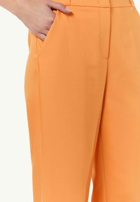 Orangene weit geschnittene Hose aus einem glatten Stoff, mit einer Fronttasche und einem minimalistischen Design ohne sichtbare Verschlüsse oder Muster.
