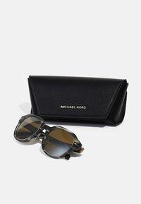 Sončna očala v črno-sivi oklepni vzorcu, z zlatimi detajli, shranjena v črni usnjeni etui s spletnim napisom "Michael Kors."
