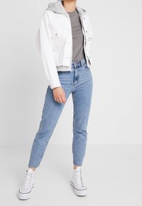 Chaqueta vaquera blanca recortada con forro gris, camiseta gris y vaqueros pitillo azul claro. Combinado con zapatillas altas blancas.