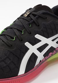 Zapatilla deportiva negra con parte superior texturizada, acentos de logotipo blancos y una suela multicolor con secciones en rosa, verde y transparentes.