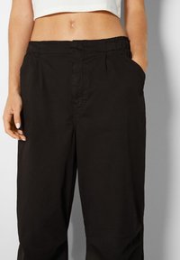 Svarta avslappnade byxor i mjukt tyg, med sidofickor, elastisk midja och subtila sömnadsdetaljer.