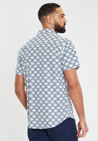Korte mouwen overhemd in het wit met een geometrisch blauw patroon. De stof is lichtgewicht met een standaard kraag en een rechte zoom.
