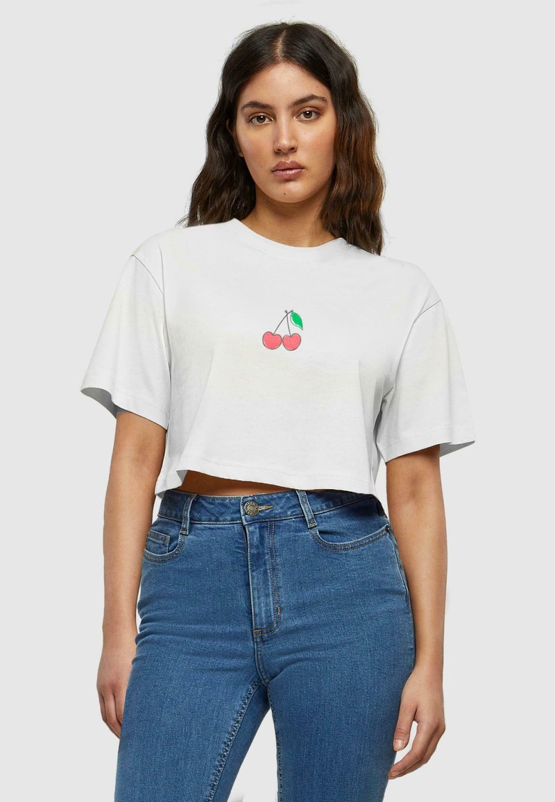 Baltos medvilnės trumpas T-shirt su mažąja rožine vyšnios grafika centre. Suderinta su aukštu liemeniu mėlynomis džinsinėmis kelnėmis.