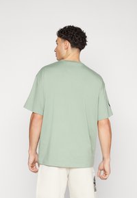 T-shirt κοντομάνικο σε ανοιχτό πράσινο βαμβακερό ύφασμα, άνετη γραμμή με στρογγυλή λαιμόκοψη, χωρίς ορατά σχέδια και απλή σχεδίαση.