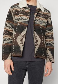 Gevoerde wollen jas met een bruin en beige geometrisch ontwerp, voorzien van een romig faux fur kraag en drukknopen.