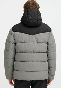 Fôret jakke med svart topppanel og grå kropp, med horisontal quiltet tekstur og hette, designet for varme og komfort.