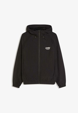 Sort lynlåsjakke med hætte, har elastiske manchetter og kant, letvægtsmateriale og en lille hvid logo på venstre bryst.