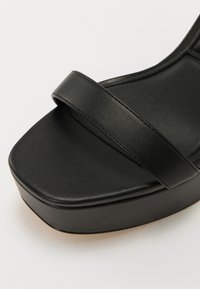 Sandale plateforme noire en cuir lisse. Dotée d'une large sangle sur l'orteil, d'une forme de bout carré solide et d'une semelle épaisse.