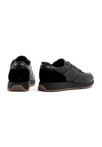 Czarne sneakersy wykonane z gładkiej skóry i zamszu, z teksturowanym wzorem, okrągłym noskiem i gumową podeszwą z brązowym akcentem.