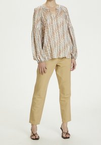 Blusa leggera e stampata in toni beige e blu, con vestibilità rilassata, maniche lunghe e scollatura a V. Abbinata a pantaloni beige slim-fit.