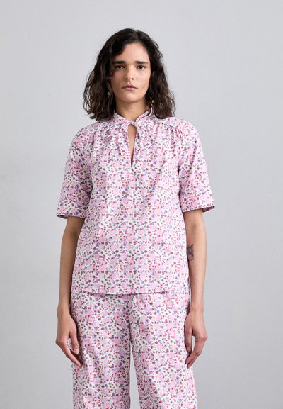 Haut à imprimé floral en rose clair, avec des manches courtes, un décolleté en trou de serrure et des détails froncés. Assorti avec un pantalon à imprimé floral coordonné.