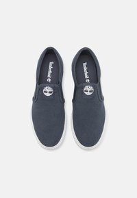 Scarpe slip-on in tela blu scuro con una suola in gomma bianca, caratterizzate da una toppa con logo rotondo su ogni tomaia e una soletta con marchio.