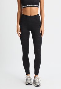 Leggings da allenamento neri con motivi astratti, vita alta e texture liscia, abbinati a un reggiseno sportivo cropped coordinato.
