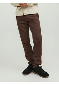 Brown cotton trousers with a straight fit, paired with black suede shoes. Light-colored jacket visible in the upper body portion.