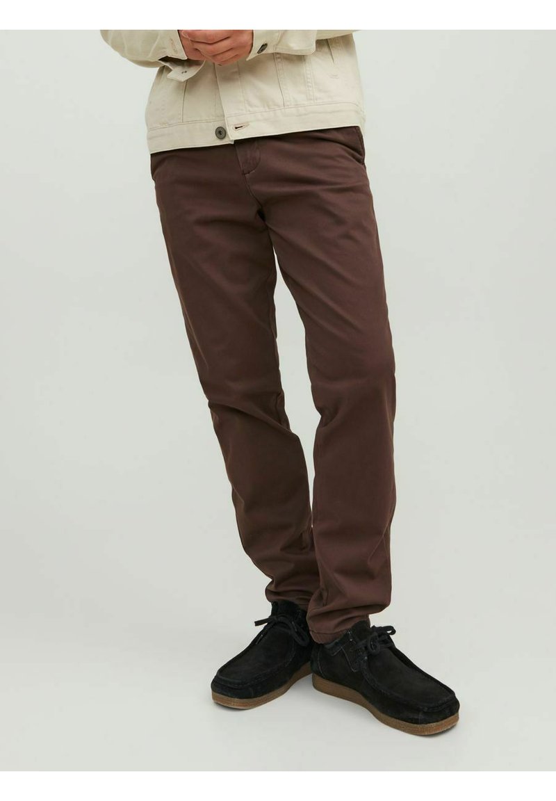 Brown cotton trousers with a straight fit, paired with black suede shoes. Light-colored jacket visible in the upper body portion.