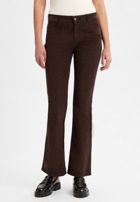 Bruine corduroy flared broek met een gladde textuur, voorzien van een knoopsluiting aan de voorkant en zijzakken, gecombineerd met zwarte schoenen.