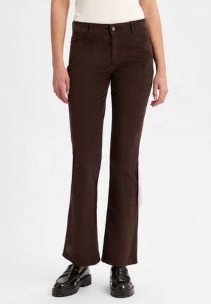 Braune Corduroy Schlaghosen mit glatter Textur, versehen mit einem Knopfverschluss vorne und seitlichen Taschen, kombiniert mit schwarzen Schuhen.