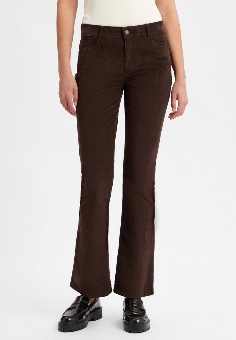 Bruine corduroy flared broek met een gladde textuur, voorzien van een knoopsluiting aan de voorkant en zijzakken, gecombineerd met zwarte schoenen.