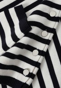 Sweter z białymi i granatowymi paskami, wykonany na drutach, z prążkowanym kołnierzem i pięcioma metalowymi guzikami wzdłuż listwy. Miękka tekstura, swobodny design.