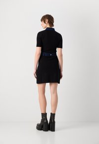 Robe noire à manches courtes avec un col en denim et une ceinture en denim assortie, présentant un corsage ajusté et un ourlet évasé, associée à des bottes à talons épais.