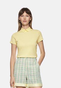 Yellow polo shirt with a collar, paired with light green checkered shorts featuring a textured pattern and cuffed hem.