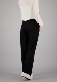 Pantalon large noir avec poches latérales, texture lisse et coupe ajustée, associé à un chemisier léger et semi-transparent.