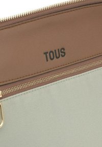 Bolso de mano con cremallera en tonos marrón y verde menta con el logo "TOUS" en negro. Superficies de cuero suave y tejido texturizado, con detalle de cremallera en tono dorado.
