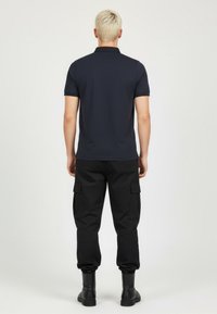 Námořnické polo tričko s krátkými rukávy a límečkem, spárované s volnými černými cargo kalhotami s bočními kapsami, vše doplněné černými botami.