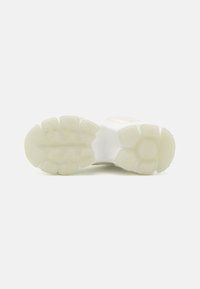 White athletic shoe sole with a textured, rubber outsole featuring circular and rectangular treads for grip. Smooth midsole in light color.