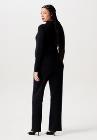 Schwarzes Langarmoberteil, kombiniert mit passenden schwarzen Hosen. Das Material wirkt weich; die Textur zeigt dezente Muster. Slim-Fit-Design mit hohen Schuhen.