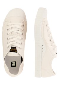 Białe płócienne trampki z gumowym noskiem, płaskimi sznurowadłami i teksturowaną podeszwą. Zawierają kontrastowe czarne logo wewnątrz.