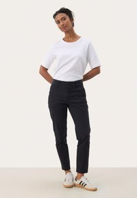T-shirt bianca a maniche corte abbinata a pantaloni sartoriali blu scuri e sneakers bianche con strisce nere. Design semplice e pulito.