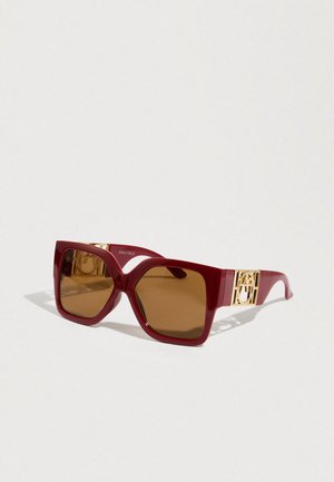 Red oversized sunglasses with a glossy finish, brown lenses, and gold-toned accent hardware on the temples. Geometric design with wide frame.