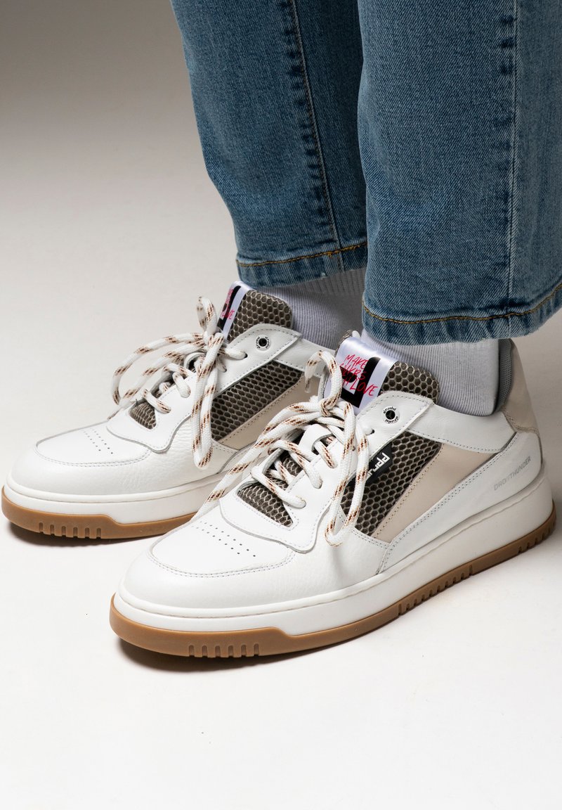 White leather sneakers featuring brown mesh accents, round laces, and a textured rubber sole. Grey detailing on the sides adds contrast.